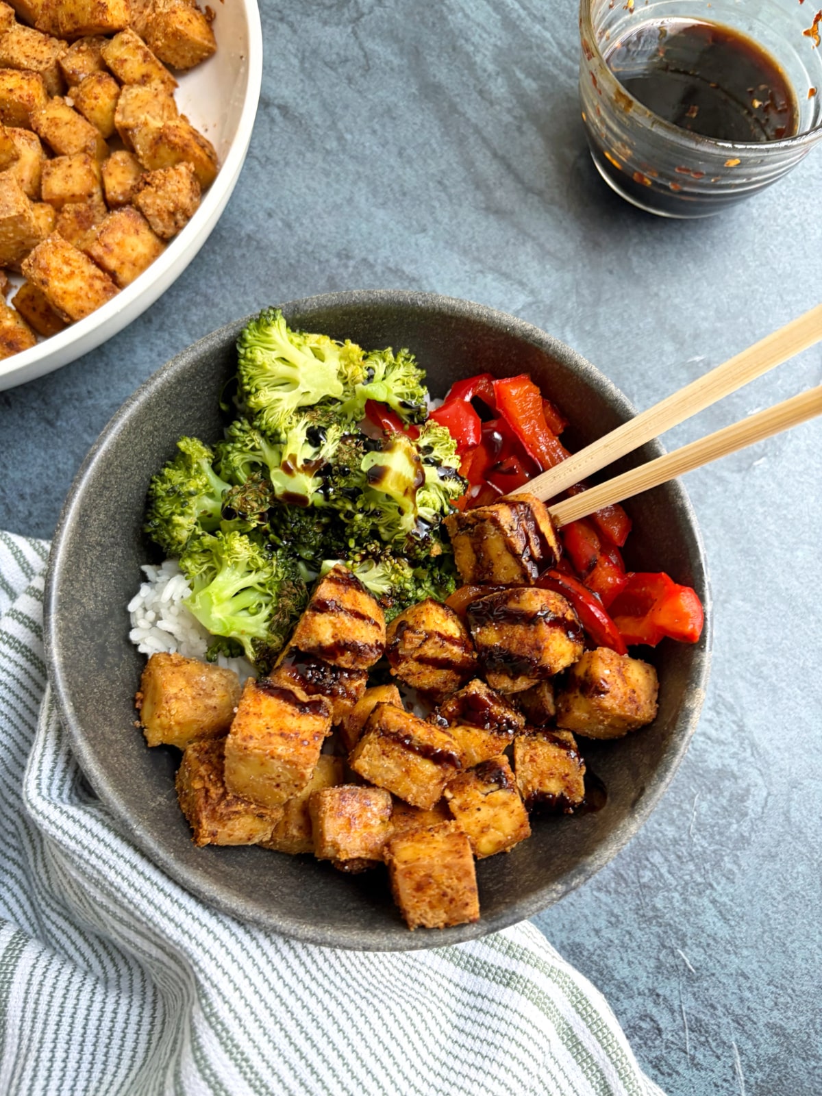 A bowl of crispy tofu, rice, and veggies with a dark soy sauce drizzled on top.