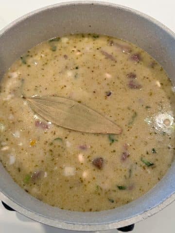 A pot filled with a tan colored liquid, beans, and a bay leaf.