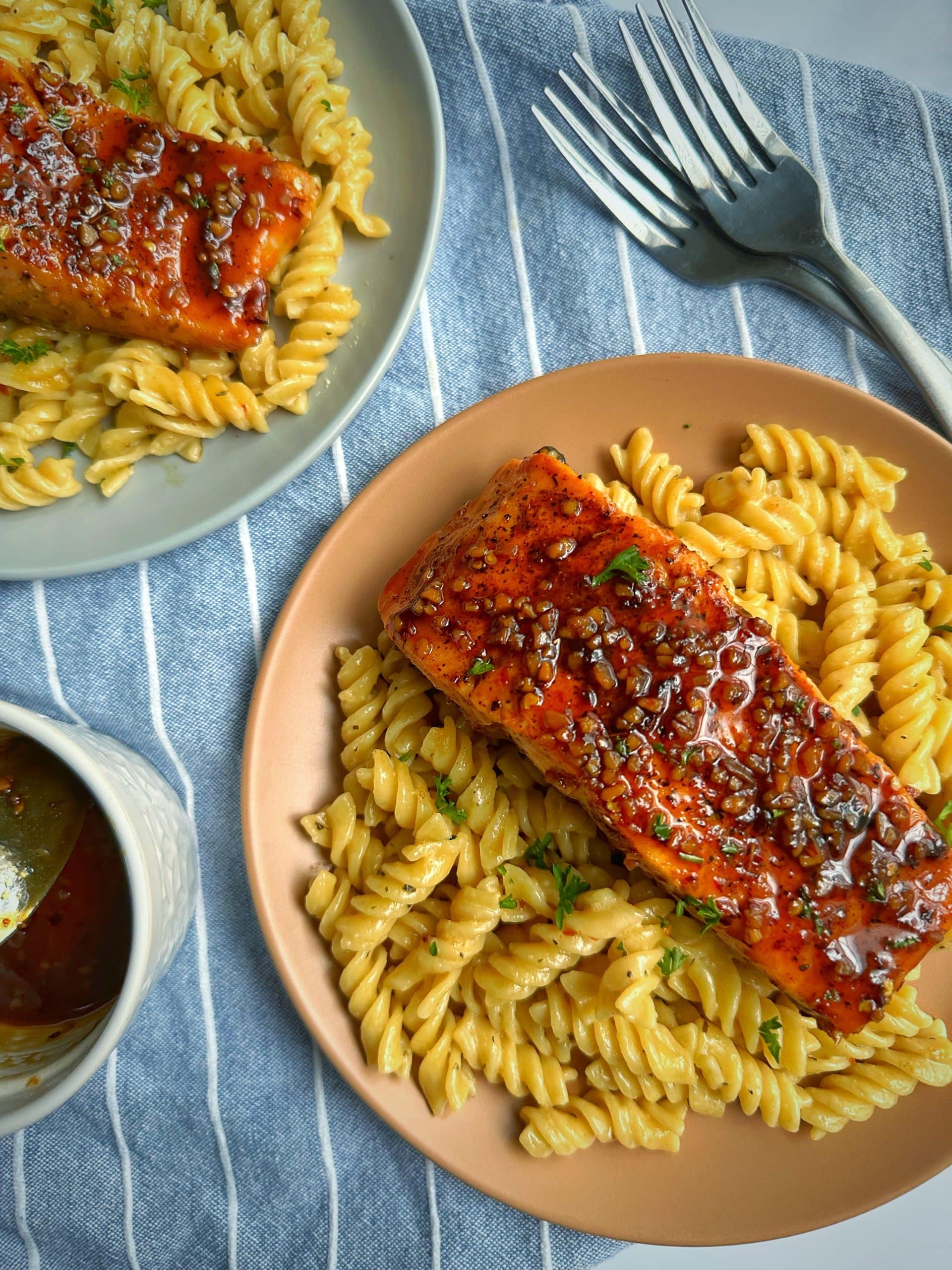 Two plates of Honey Soy Salmon over creamy pasta with more honey soy sauce on the side.