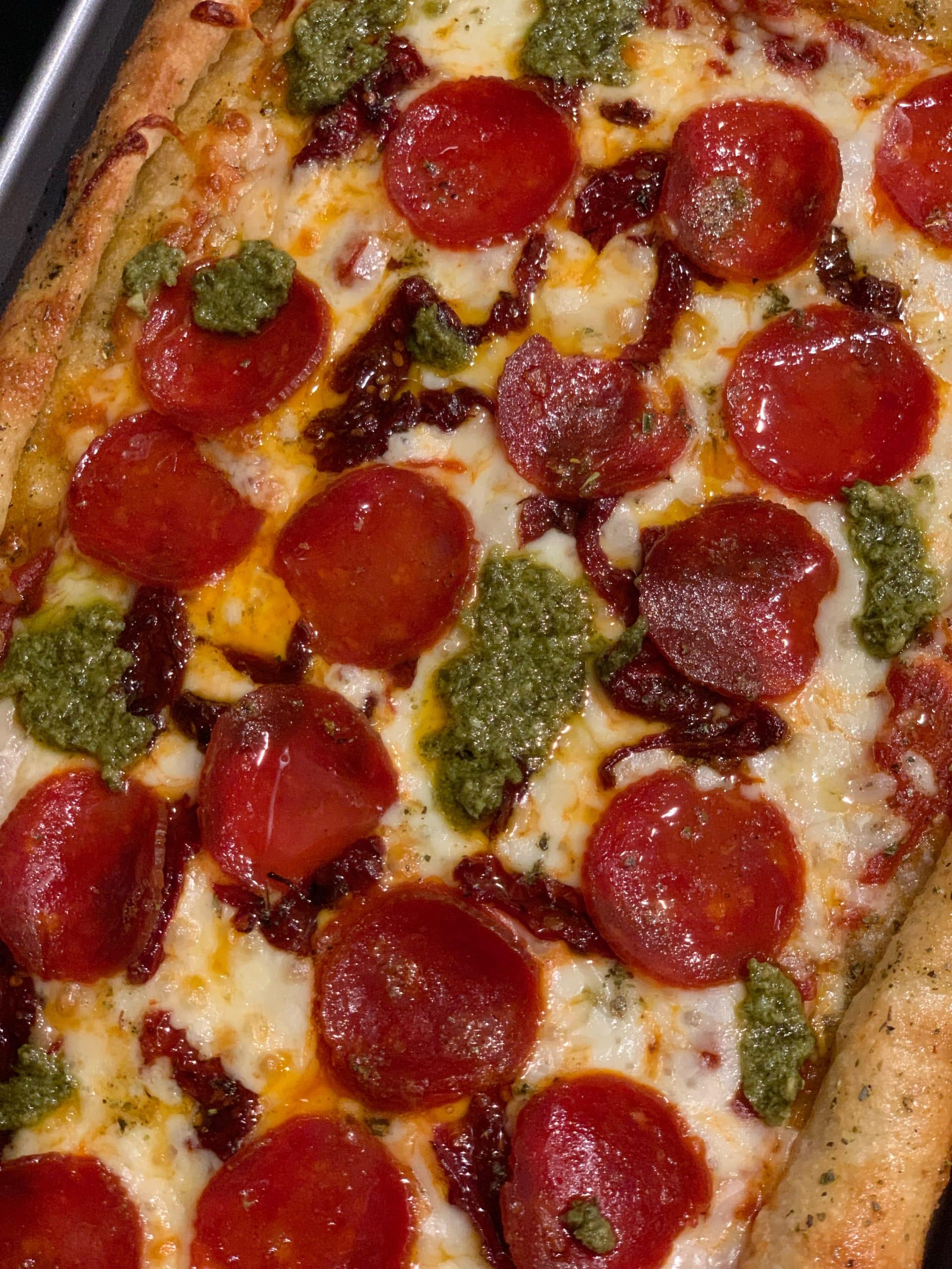 A picture of a personal pan pizza with pepperoni, sun-dried tomatoes, and pesto.