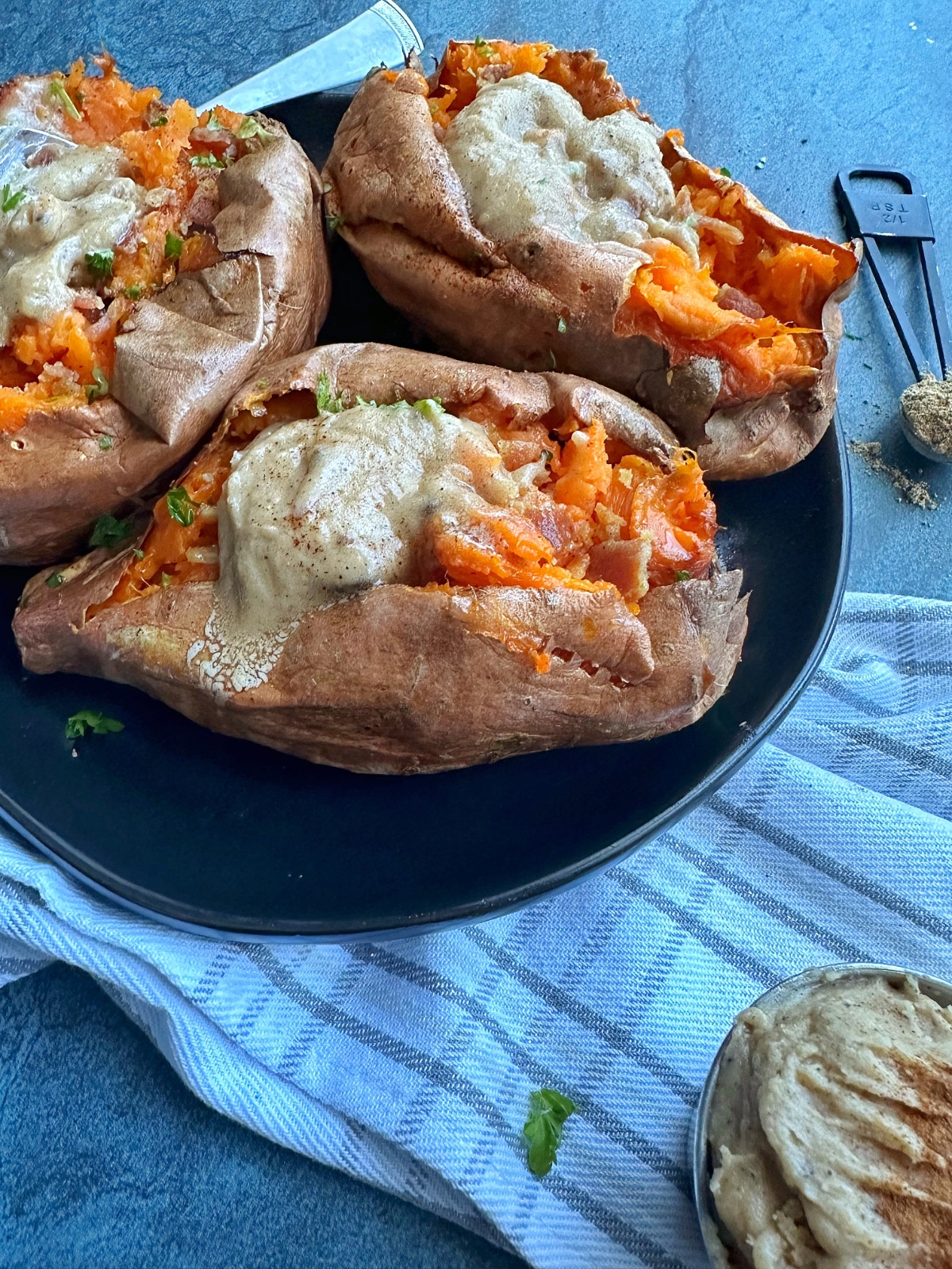 Three baked sweet potatoes on a black plate, topped with chai butter.