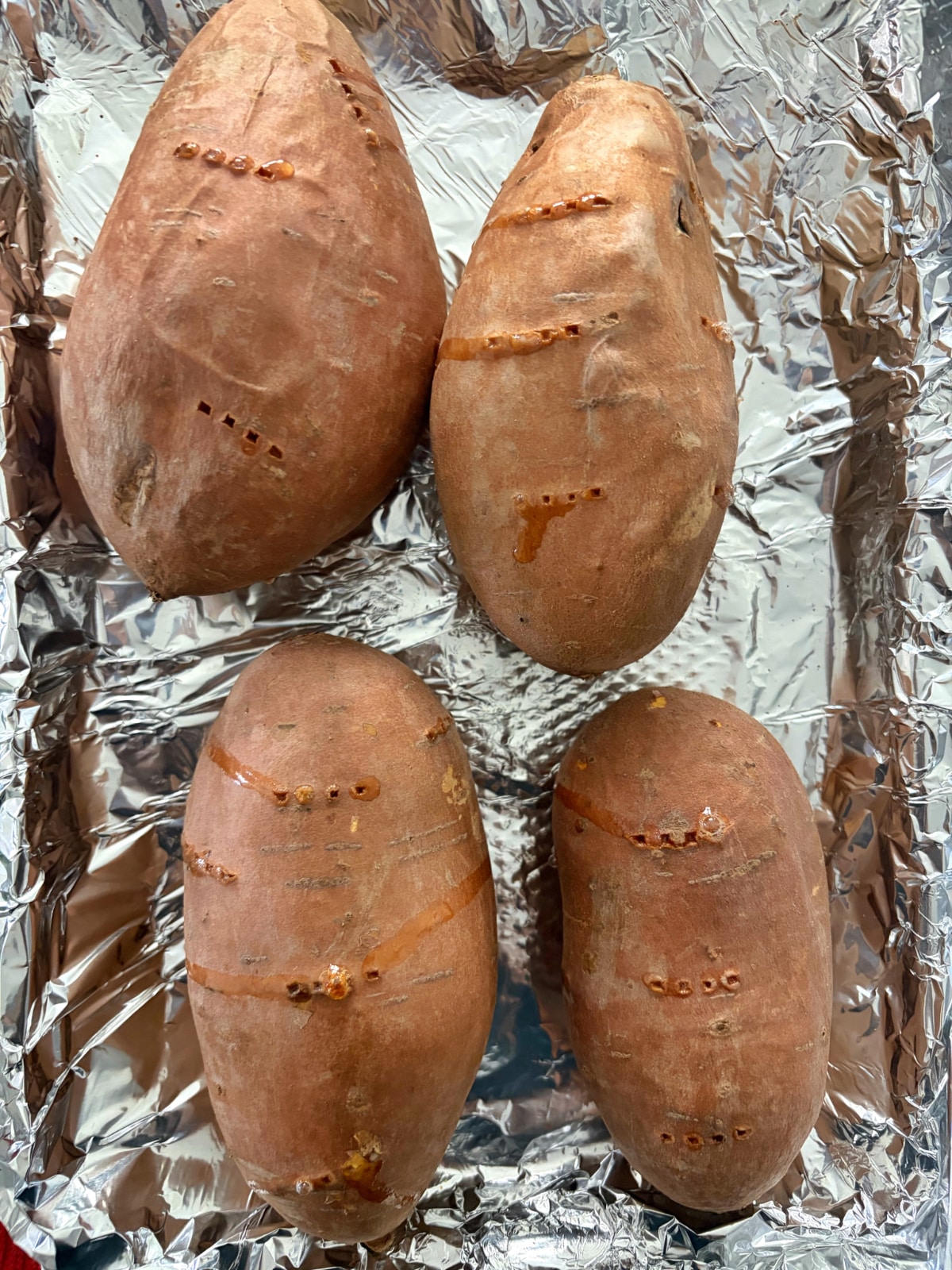 A foil-lined pan filled with 4 baked sweet potatoes.