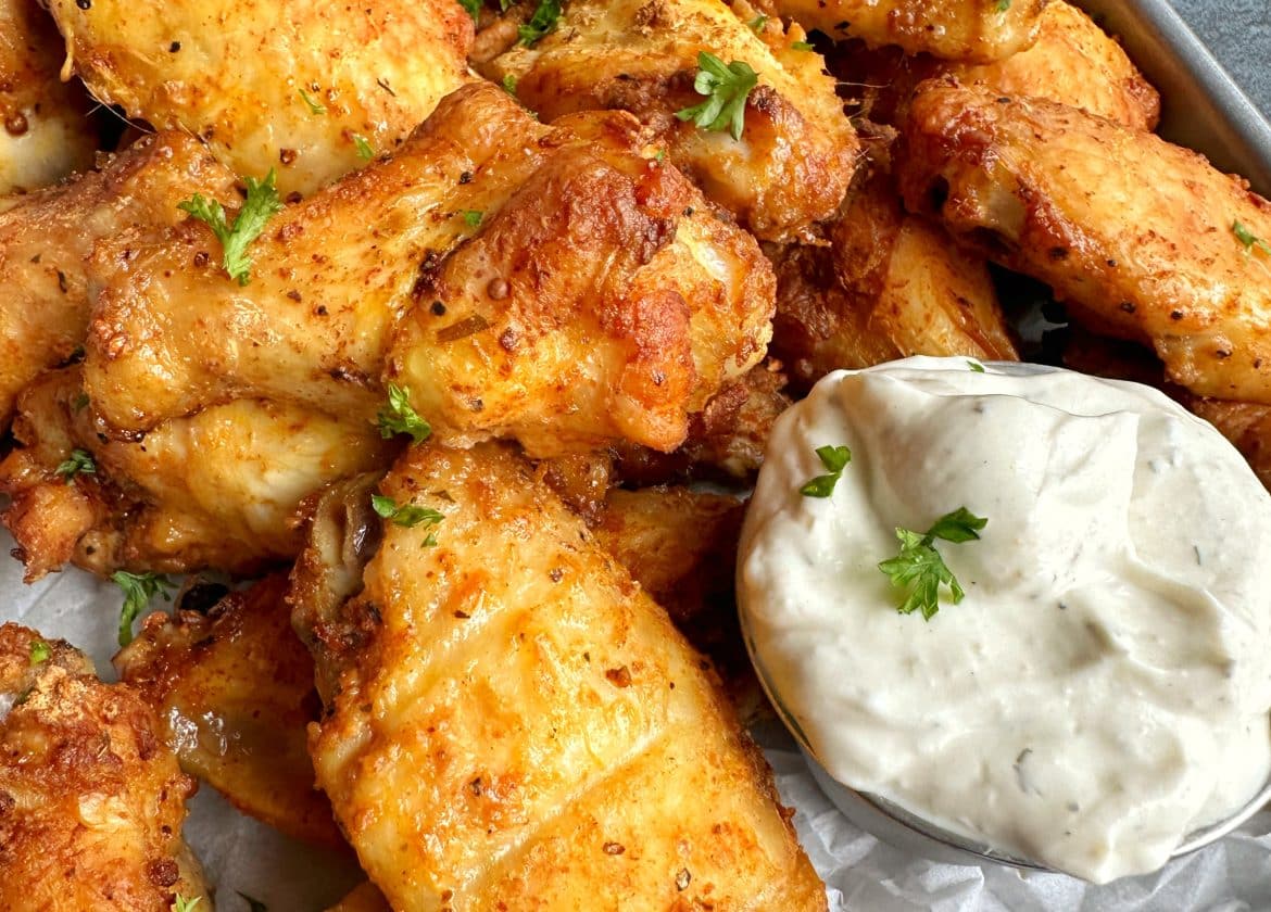 A tray of crispy oven-baked chicken wings with a cup of homemade ranch and celery sticks.