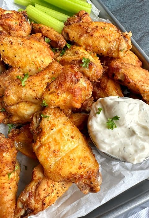 A tray of crispy oven-baked chicken wings with a cup of homemade ranch and celery sticks.