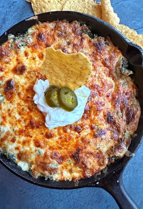 A cast-iron skillet filled with creamy hot spinach dip, with sour cream and jalapeños on top.