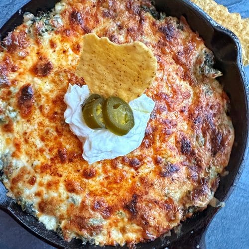 A cast-iron skillet filled with creamy hot spinach dip, with sour cream and jalapeños on top.