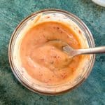 A spoon dipped into a bowl of orange bang bang sauce.