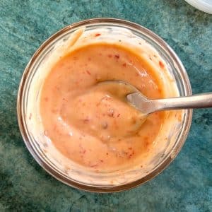 A spoon dipped into a bowl of orange bang bang sauce.
