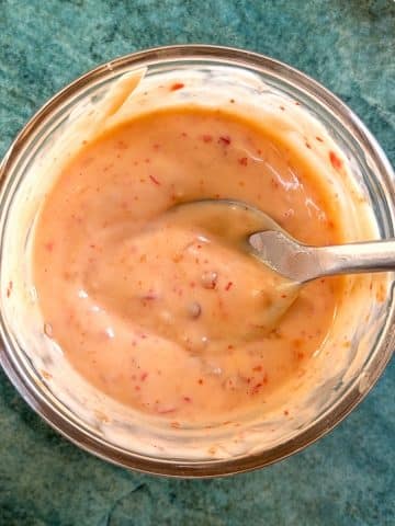 A spoon dipped into a bowl of orange bang bang sauce.