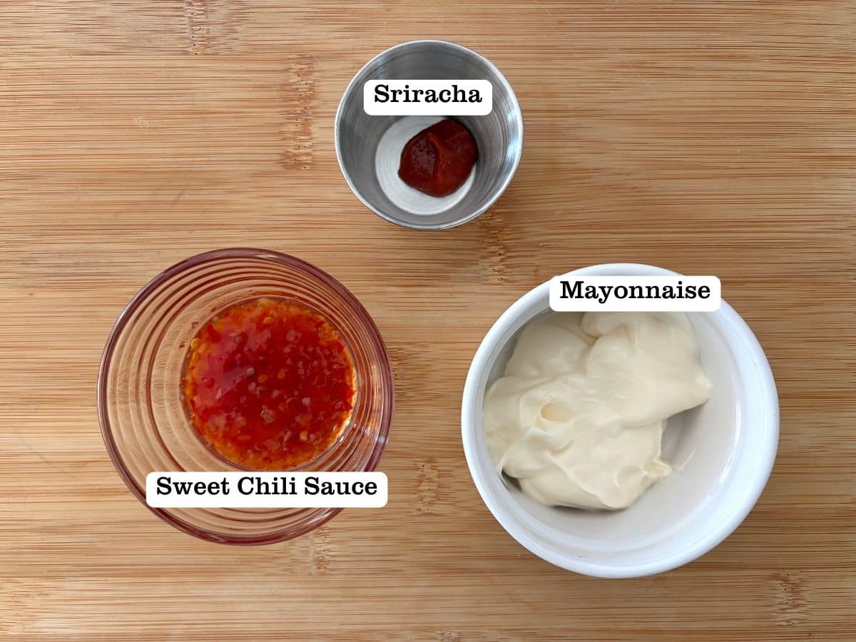A wooden board with bowls of sweet chili sauce, mayo, and sriracha.