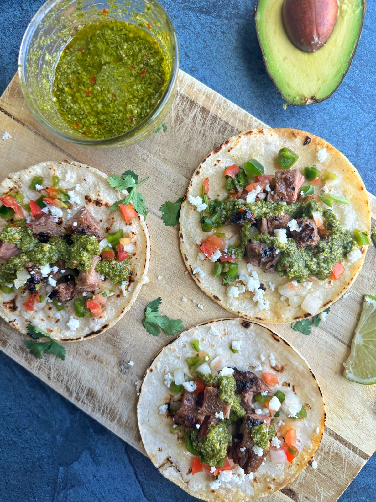 A wooden board topped with chimichurri flank steak tacos.