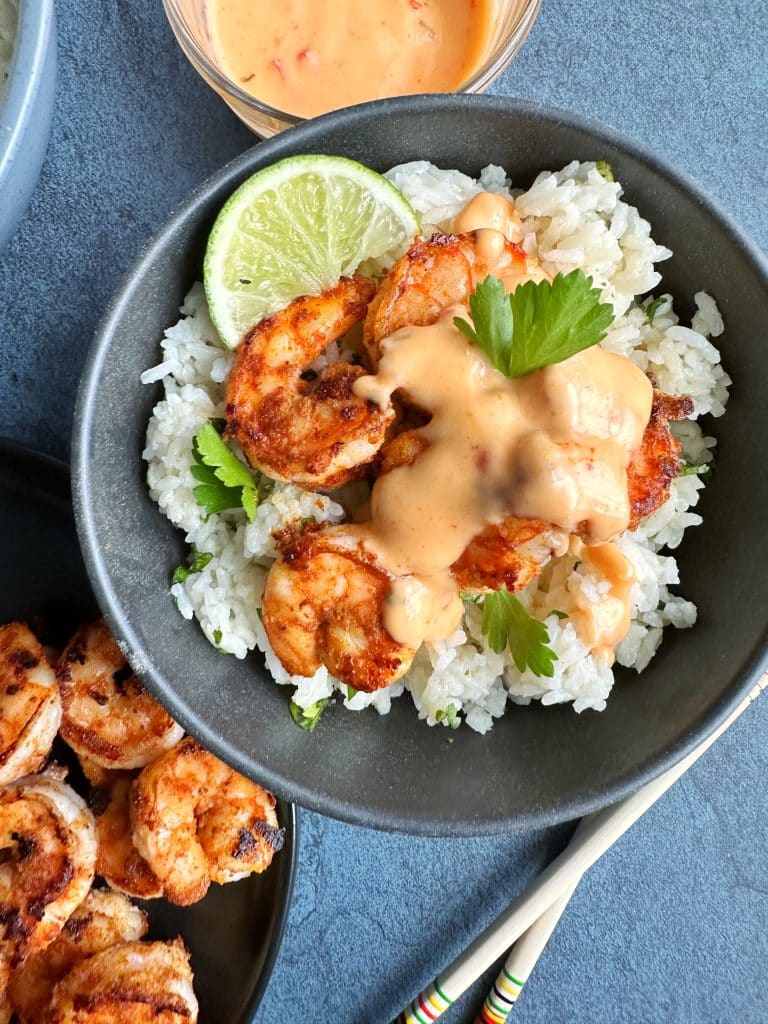 A bowl of Grilled Bang Bang Shrimp over cilantro-lime rice with a lime on the side.