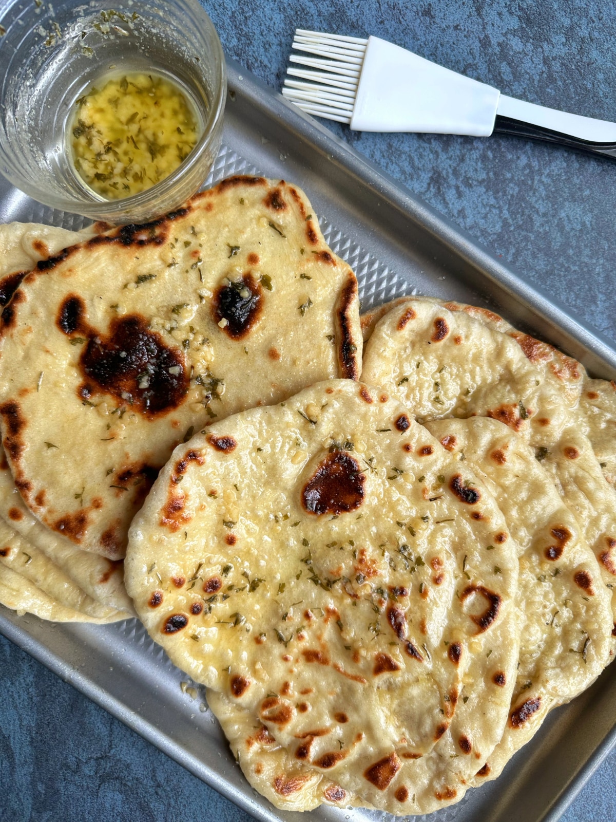 A Sheet pan of homemade garlic naan bread with garlic-butter sauce on the side.