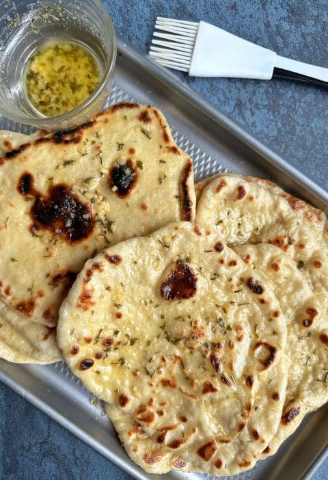 A tray of homemade garlic naan bread with garlic-butter sauce and a pastry brush on the side.