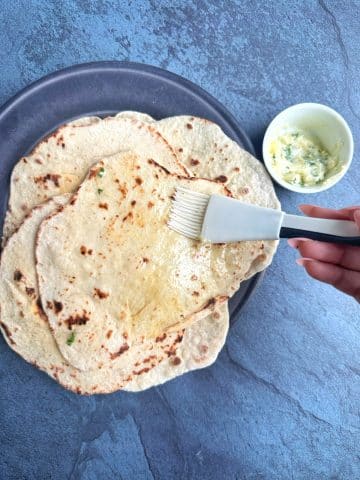 A hand using a basting brush to spread garlic butter onto pieces of naan.