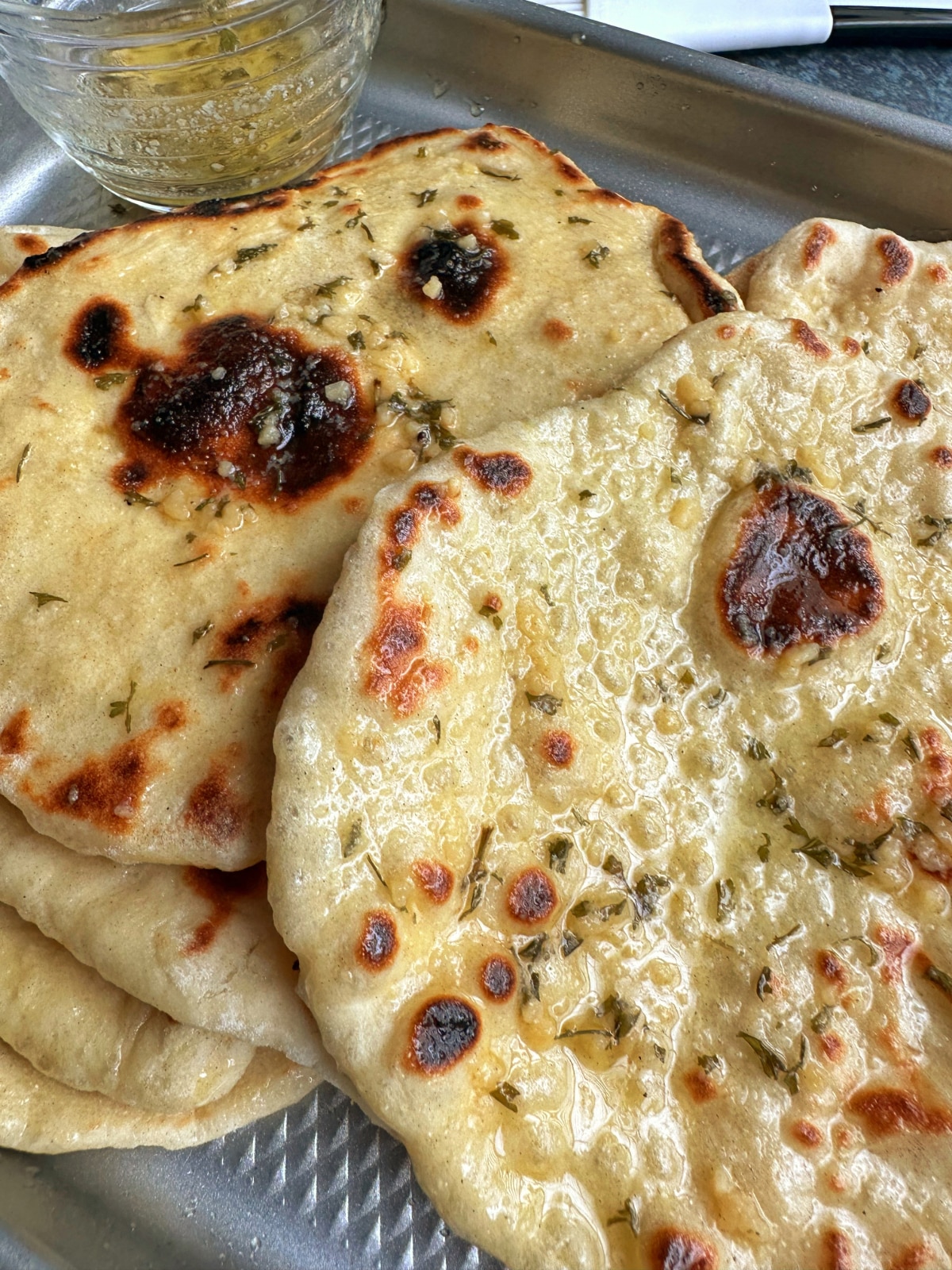 Homemade garlic naan on a sheet pan with garlic butter in a saucer on the side.