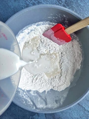 Pouring milk into a mixing bowl filled with flour and yeast.