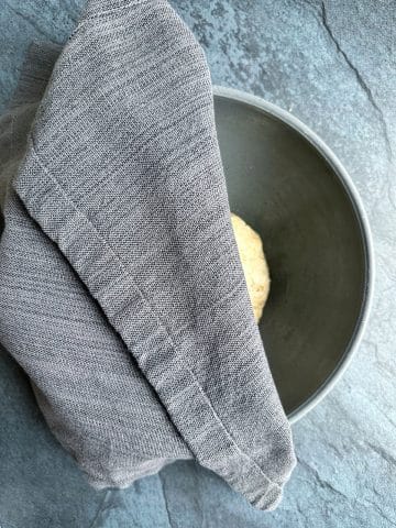 A kitchen towel partially covering a mixing bowl filled with a ball of dough.