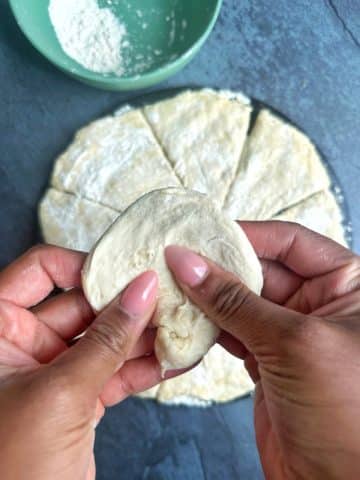 Hands shaping naan dough into a disc.
