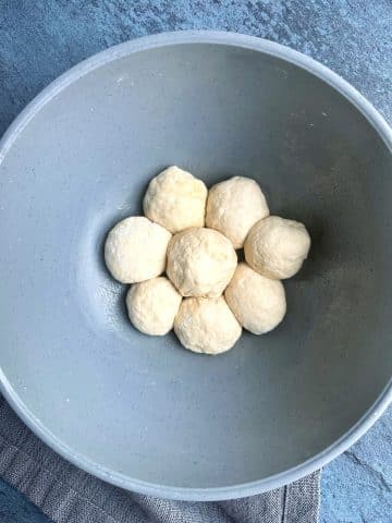 A mixing bowl containing eight balls of bread dough.