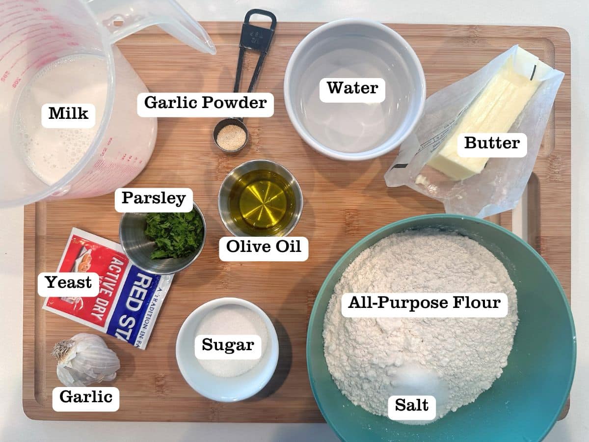A wooden board containing ingredients to make naan bread, including yeast, flour, and milk.
