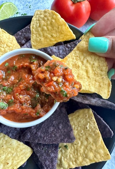 A hand dipping a yellow corn chip into a bowl of estaurant-style, homemade fire roasted salsa.