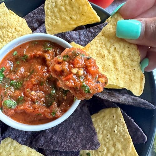 A hand dipping a yellow corn chip into a bowl of estaurant-style, homemade fire roasted salsa.