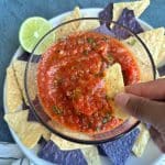 A hand dipping a tortilla chip into fire roasted salsa