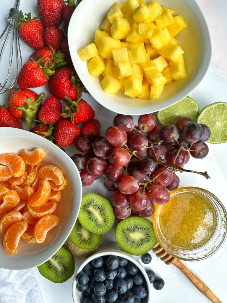 The ingredients for rainbow fruit salad spread out on a board with a sauce bowl of agave-lime syrup on the side.