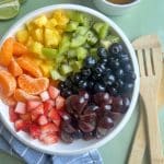 A bowl of fruit salad with kiwi, pineapple, oranges, berries, and grapes.