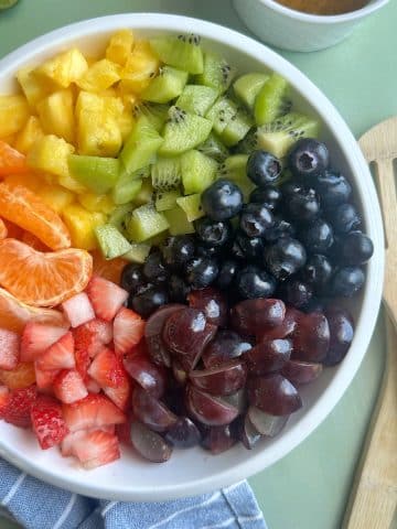 A bowl of fruit salad with kiwi, pineapple, oranges, berries, and grapes.