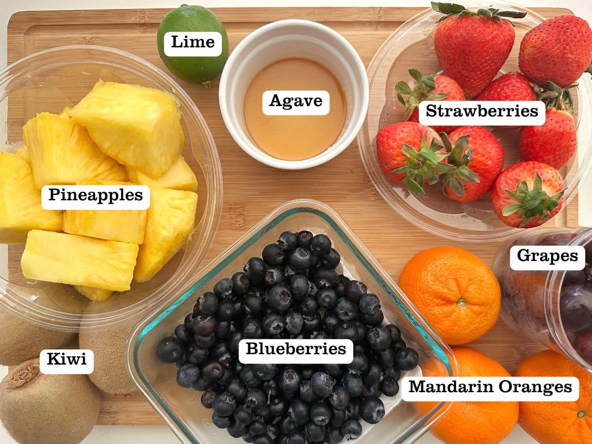 A wooden board containing bowls of fresh fruit and agave syrup.