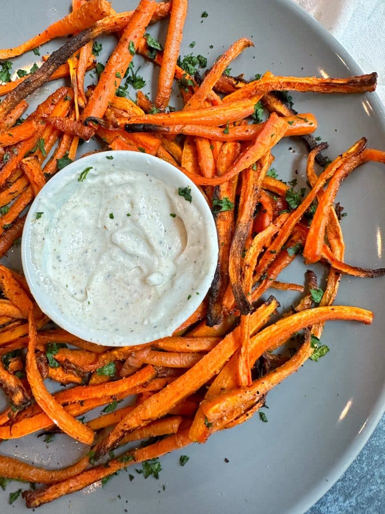 A bowl of crispy baked carrot fries served with a white dipping sauce.