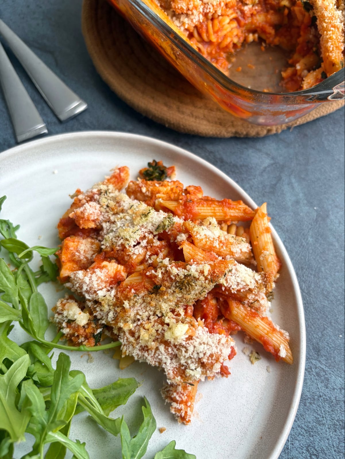 A plate filled with chicken parmesan pasta bake with an arugula salad on the side.