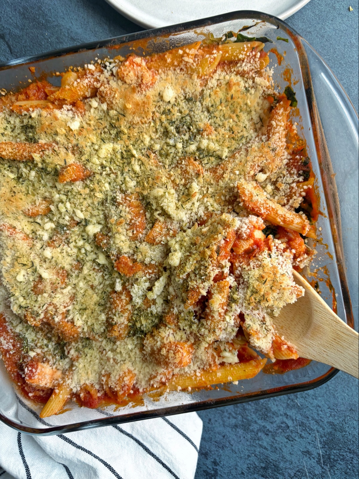 A baking dish filled with tomato pasta bake, with a wooden spoon sticking out of the side.