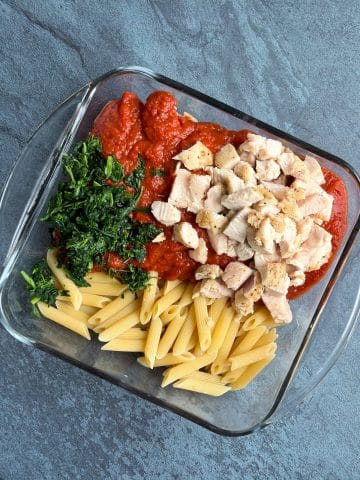 A glass baking dish filled with pasta, sauce, chopped chicken, and spinach.