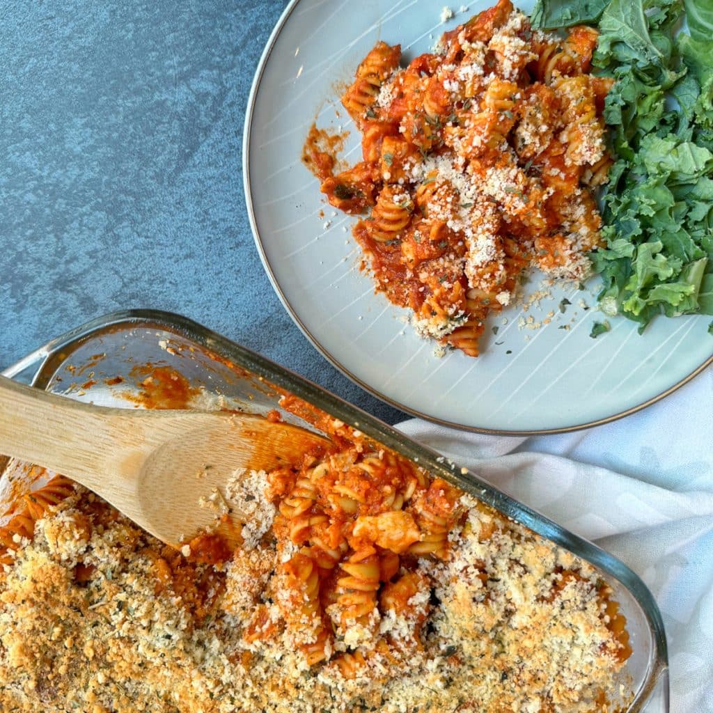 A serving of chicken parmesan casserole with kale salad on the side and the leftovers in a baking dish.