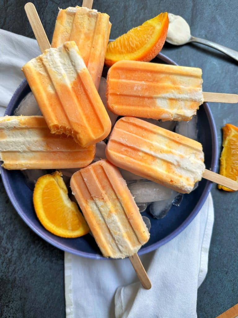A bowl of homemade orange creamsicles sitting on top of ice with orange slices in the background.