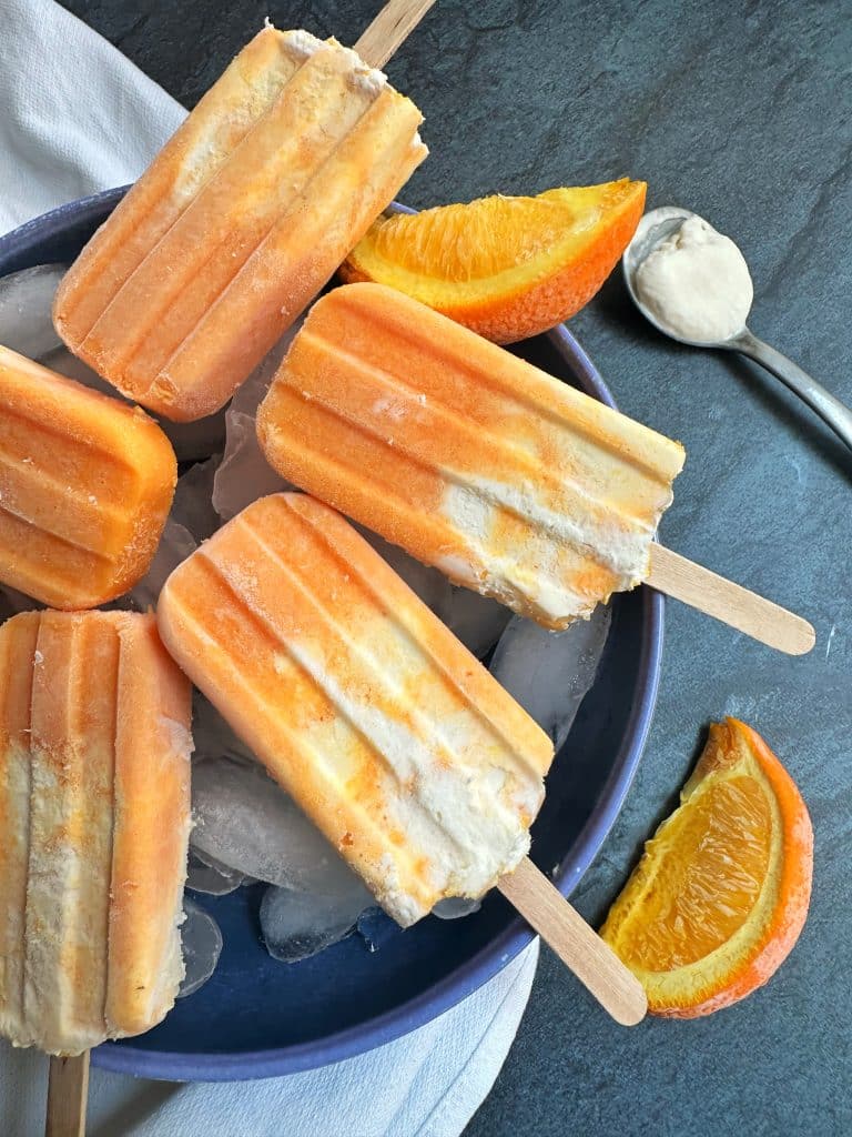 A bowl of homemade orange creamsicles sitting on top of ice with orange slices in the background.