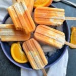 A bowl of homemade orange creamsicles sitting on top of ice with orange slices in the background.
