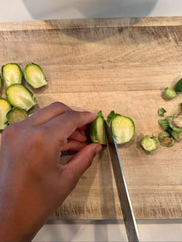 Two hands slicing a fresh brussels sprout into halves.