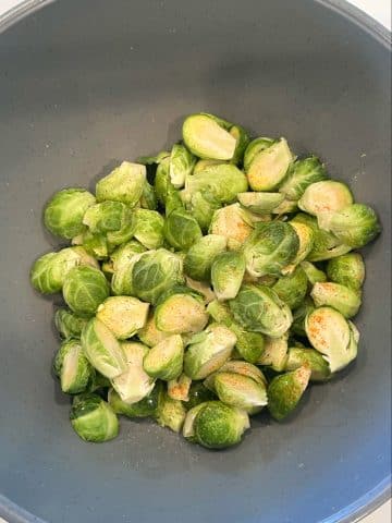 A mixing bowl filled with trimmed brussels sprouts, salt, cayenne, and vegetable oil.