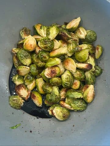 A mixing bowl filled with roasted brussels sprouts, balsamic vinegar, and honey before tossing together.