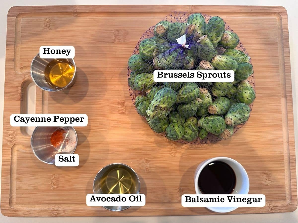 A wooden board containing the ingredients for roasted brussels, including avocado oil and honey.