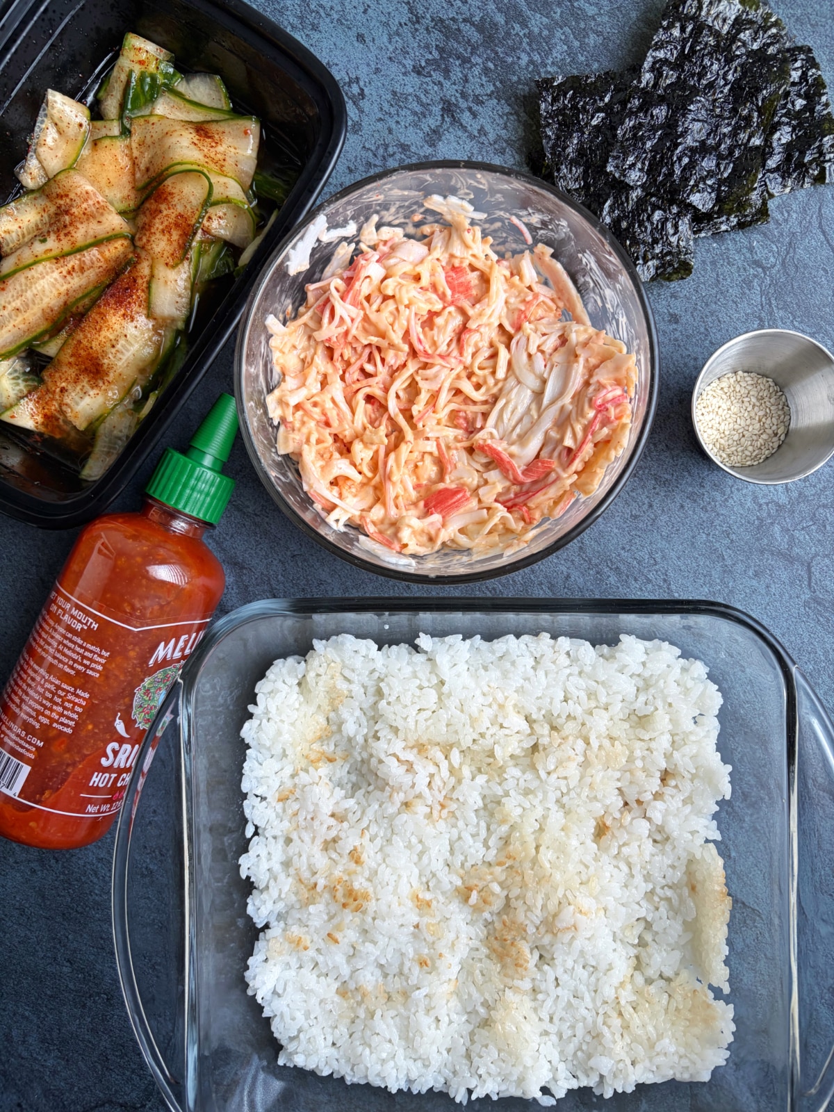 A flatlay photo with all of the prepared ingredients to make a layered sushi casserole.