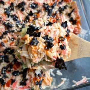 A wooden spoon holding up a portion of sushi bake over the rest of the pan.