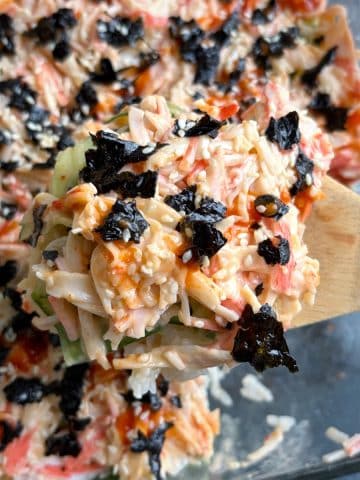 A wooden spoon holding up a portion of sushi bake over the rest of the pan.