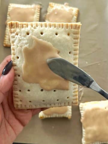 Brown icing being spread on top of a baked pastry.