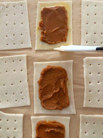 Egg wash being brushed onto the edges of pie crust rectangles filled with pumpkin filling.