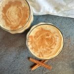 An overhead shot of two glasses of dairy free eggnog made with oat milk, with cinnamon sticks on the side.